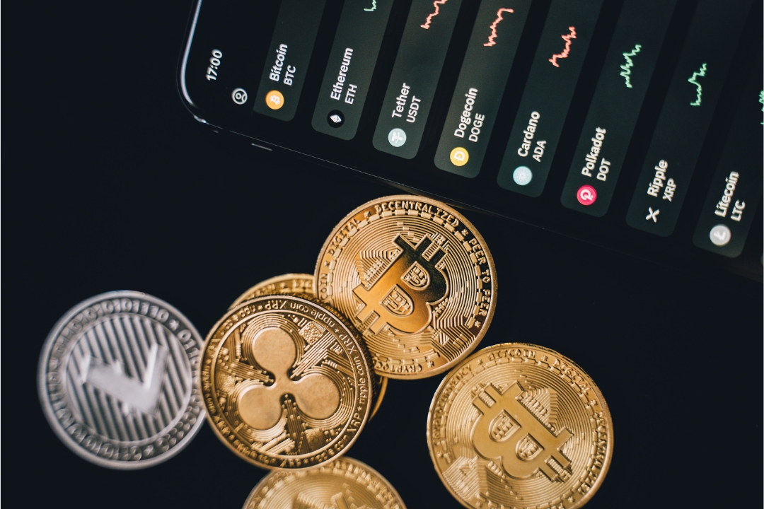 Golden Bitcoin and Ripple coins with live crypto price chart on smartphone screen showing BTC, ETH, and DOGE prices – representing the crypto market surge during U.S. Crypto Week 2025