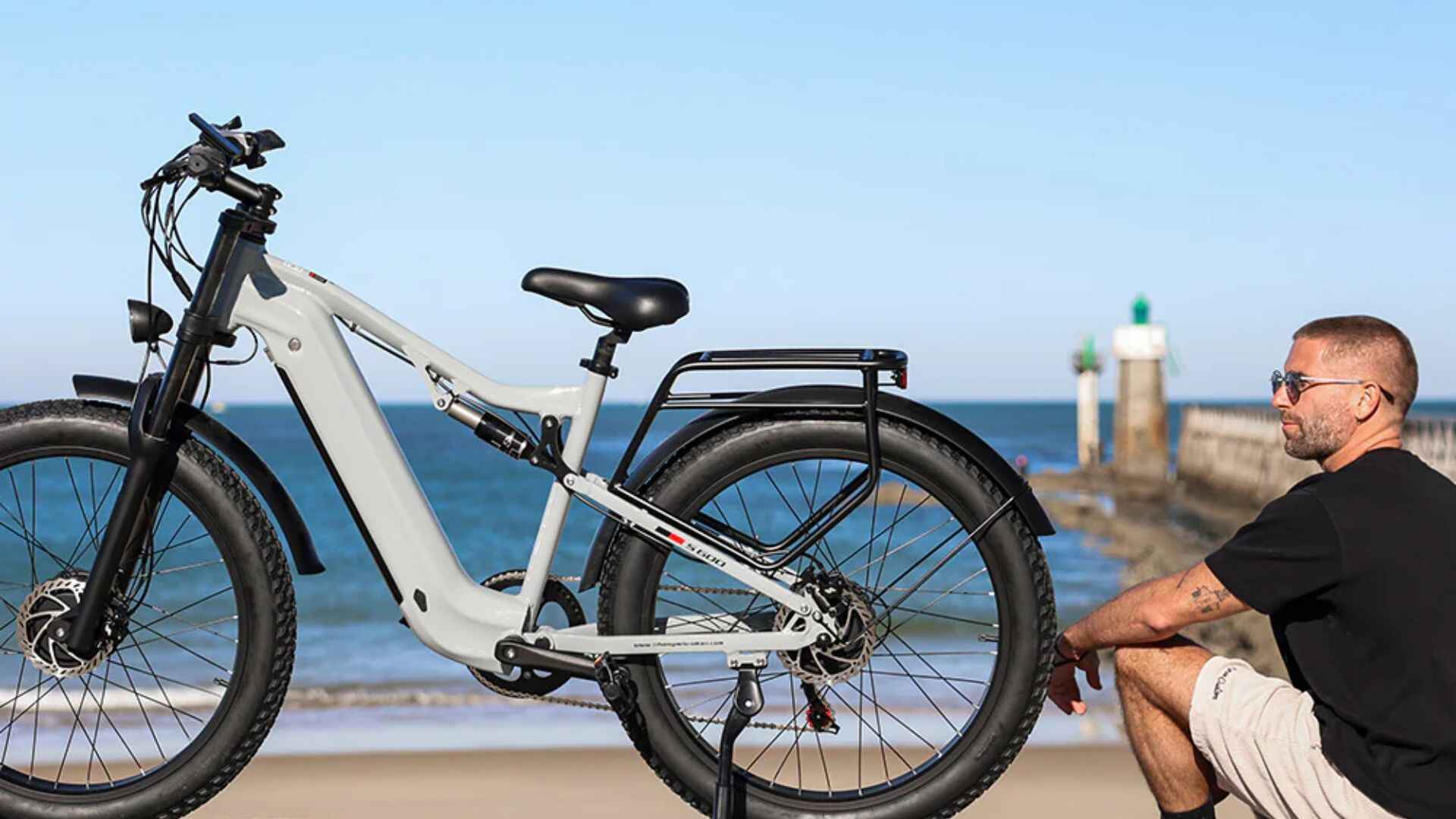 A man sitting by the beach with an electric bike, representing performance and reliability powered by the perfect electric bike charger.