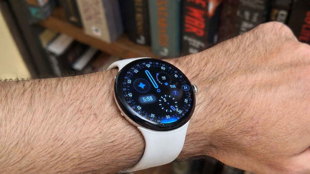 Google Pixel Watch 4 on wrist showing Wear OS 6.0 interface with customizable watch face and smart widgets.
