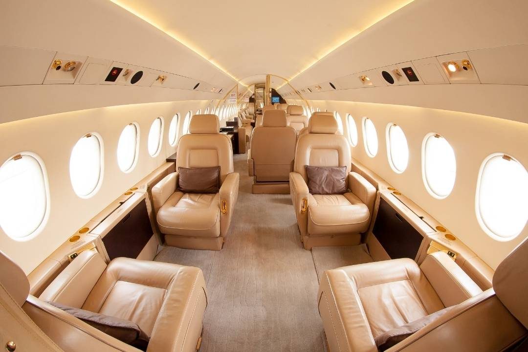 Four Seasons Private Jet Interior of a luxurious private jet, featuring beige leather reclining seats with pillows, soft lighting, and a spacious aisle, creating a sophisticated and comfortable travel environment. Four Seasons Private Jet